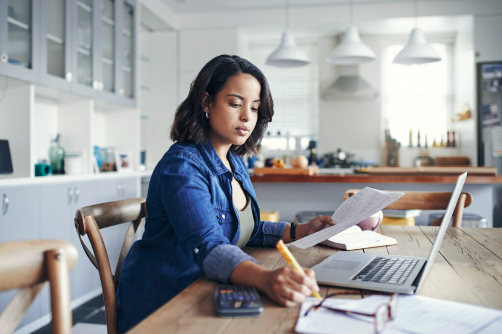 Woman using a laptop while calculating and going through her budget and spending - showing a concept of proper investing.
